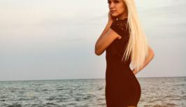Blonde in little black dress is on the beach 